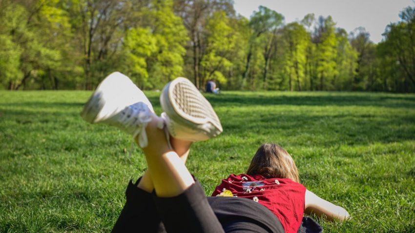 woman in black pants and red shirt lying on green grass field during daytime